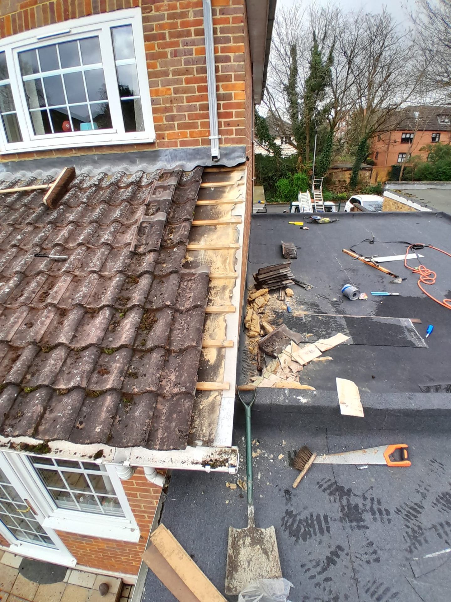 Tile strip in progress next to flat roof — repair works